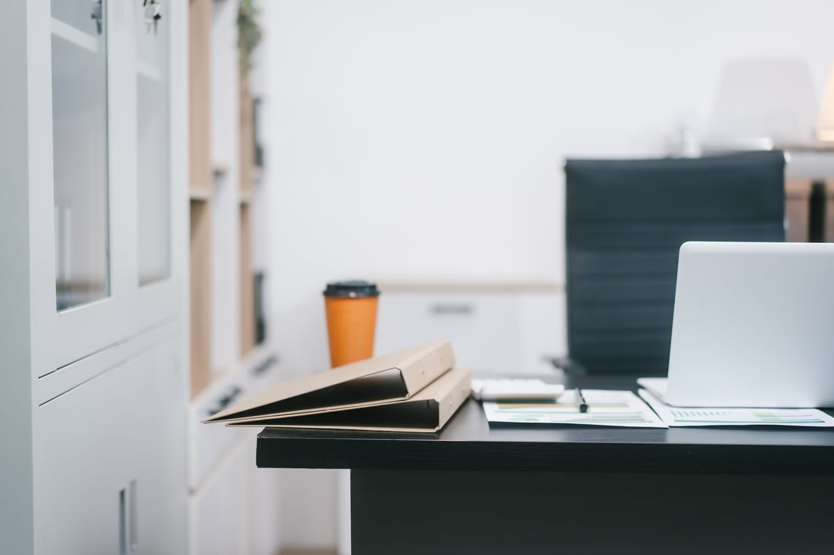 A modern office workspace with a black desk, documents, a coffee cup, and a laptop