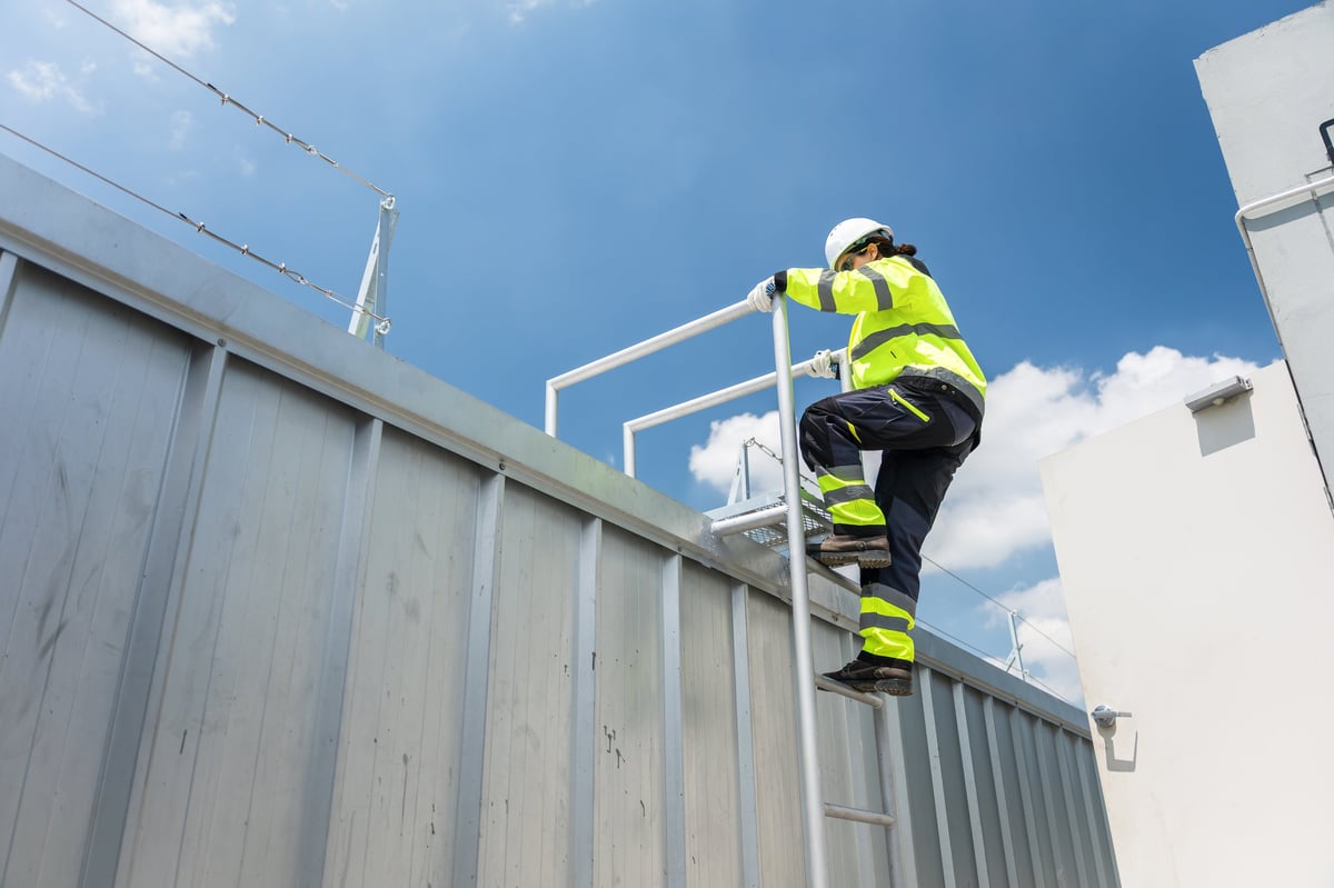 Female engineer climbing a metal ladder for technical installation at construction site