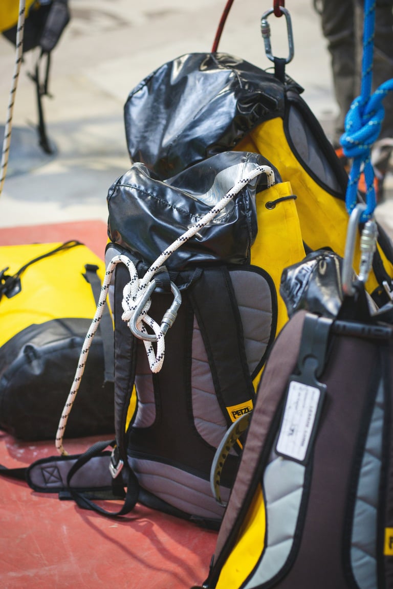 Rock climbing harness with yellow backpack and coiled white rope attached to carabiners, suspended outdoors